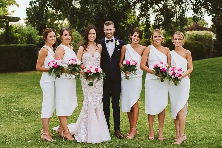 Groom posing with the bride and five women holding pink and white bouquets.