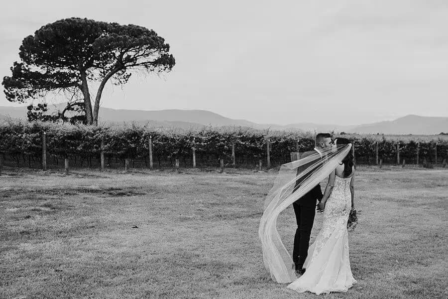 Black-and-white portrait of the couple embracing as the bride's veil blows beside them.