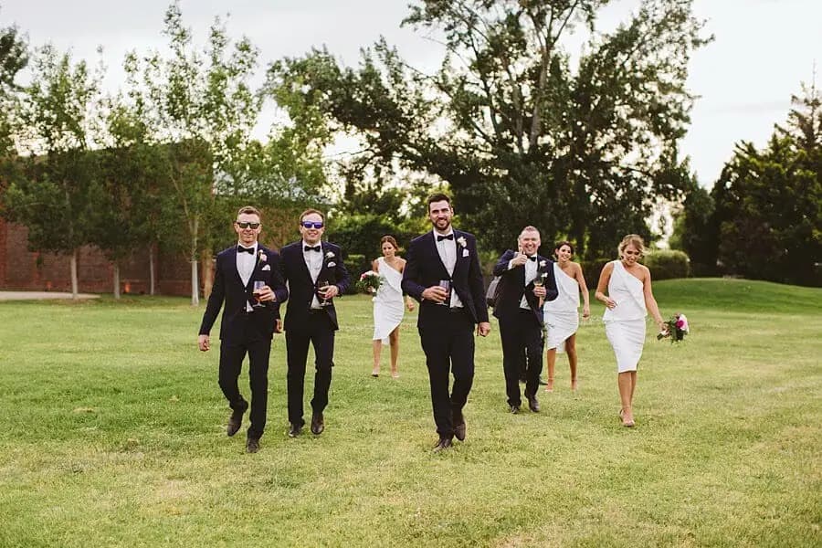 Wedding party walking across the lawn in dark suits and white dresses.