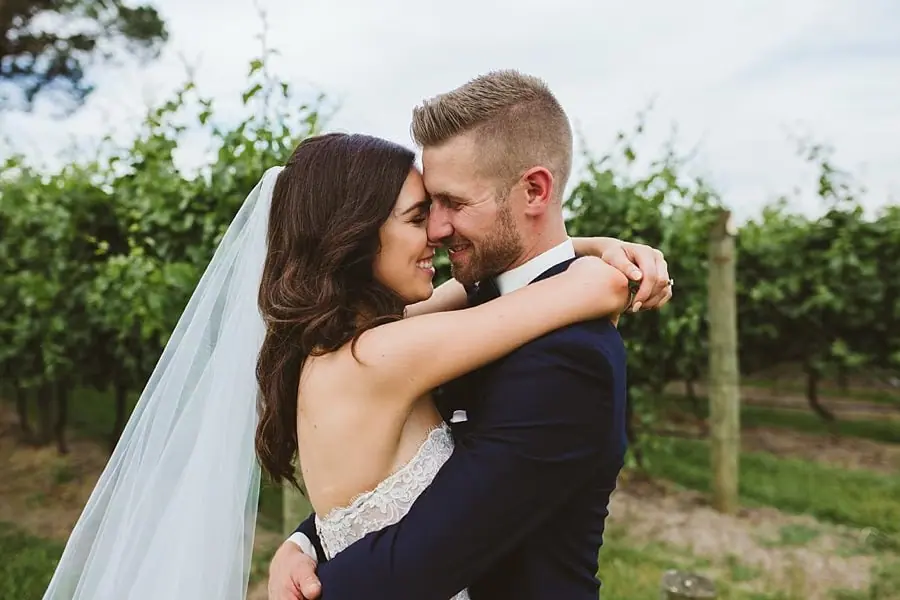 Bride and groom embracing closely between vineyard rows.