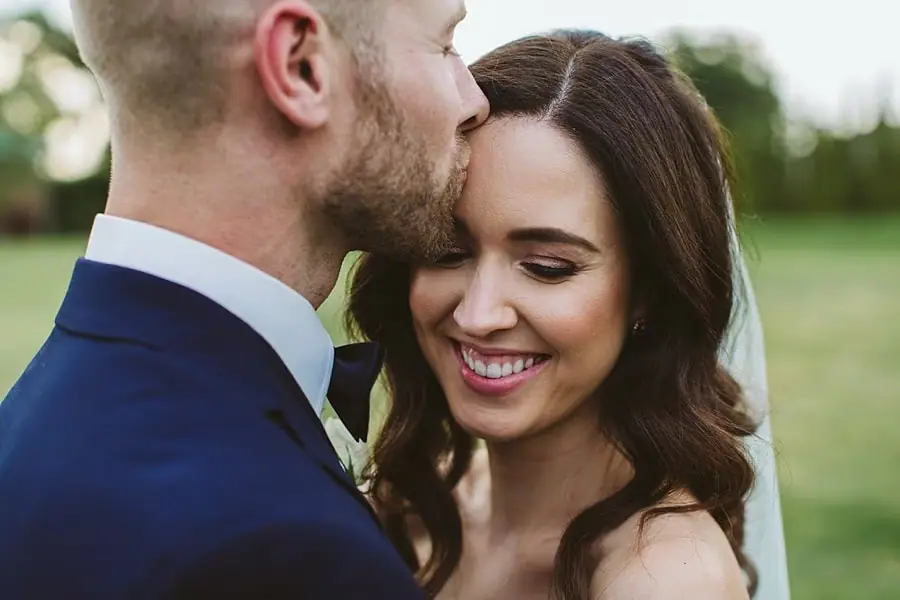 Groom kissing the smiling bride's forehead in the vineyard.