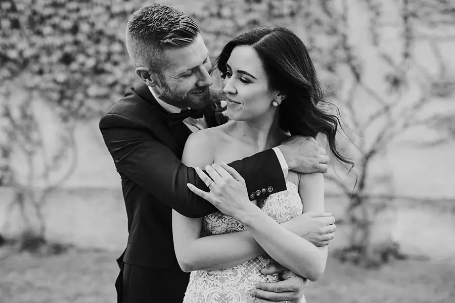 Black-and-white portrait of the groom embracing the bride from behind.