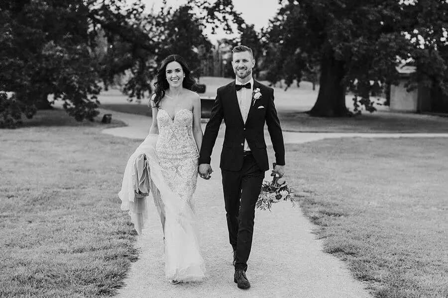 Black-and-white photograph of the couple walking hand in hand along a garden path.
