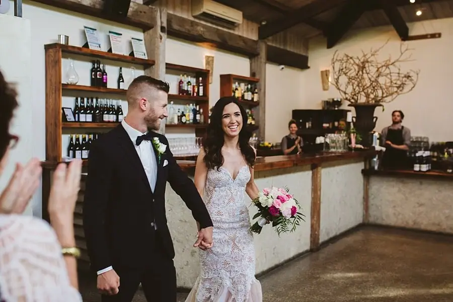 Bride and groom entering the reception holding hands and smiling.