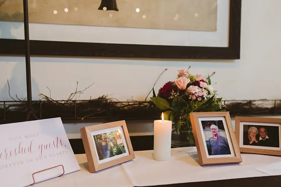 Framed photographs, a candle and flowers arranged on a white memorial table.