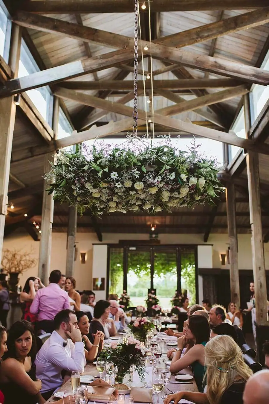 Guests seated beneath timber beams and a large hanging floral arrangement.