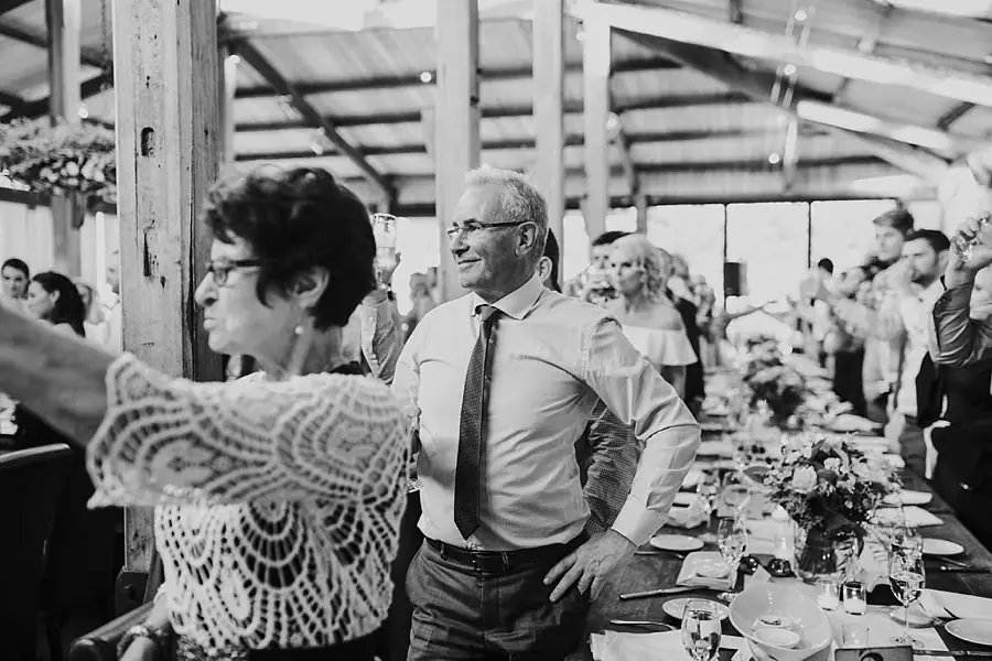 Black-and-white photograph of a man standing among guests at a long reception table.