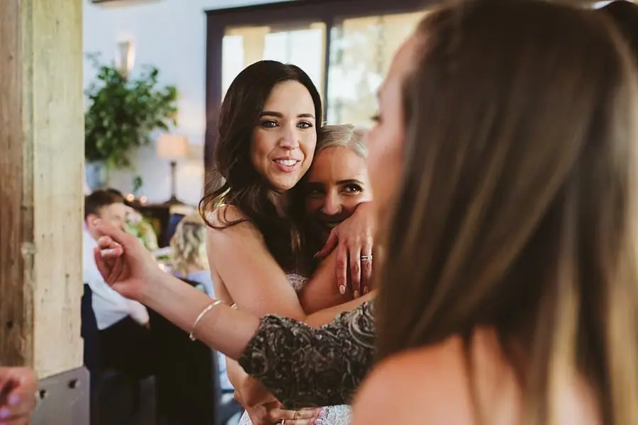 Bride smiling while embracing a guest among companions at the reception.