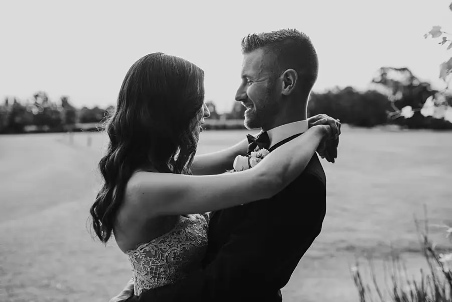 Black-and-white portrait of the couple smiling at each other on the lawn.