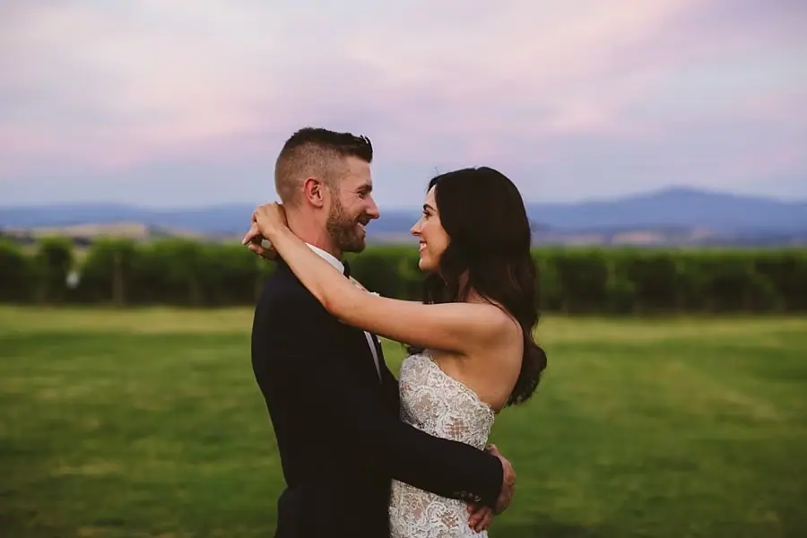 Bride and groom smiling at each other while embracing at dusk.