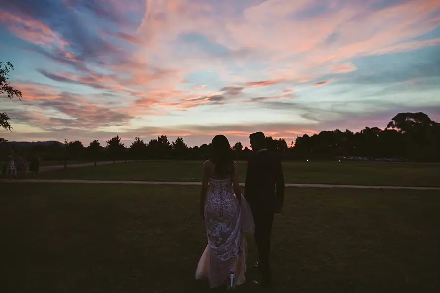 Couple silhouetted on the lawn beneath sweeping pink and blue sunset clouds.