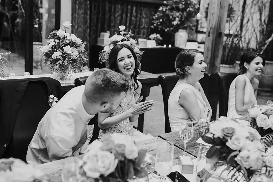 Black-and-white photograph of the bride laughing and clapping beside the groom.