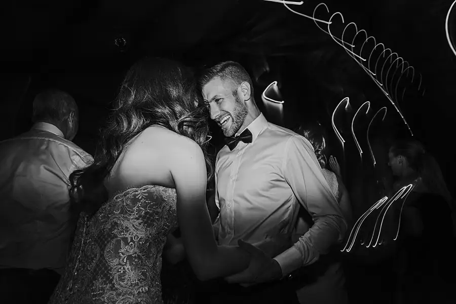 Black-and-white photograph of the bride and groom dancing beneath streaks of light.