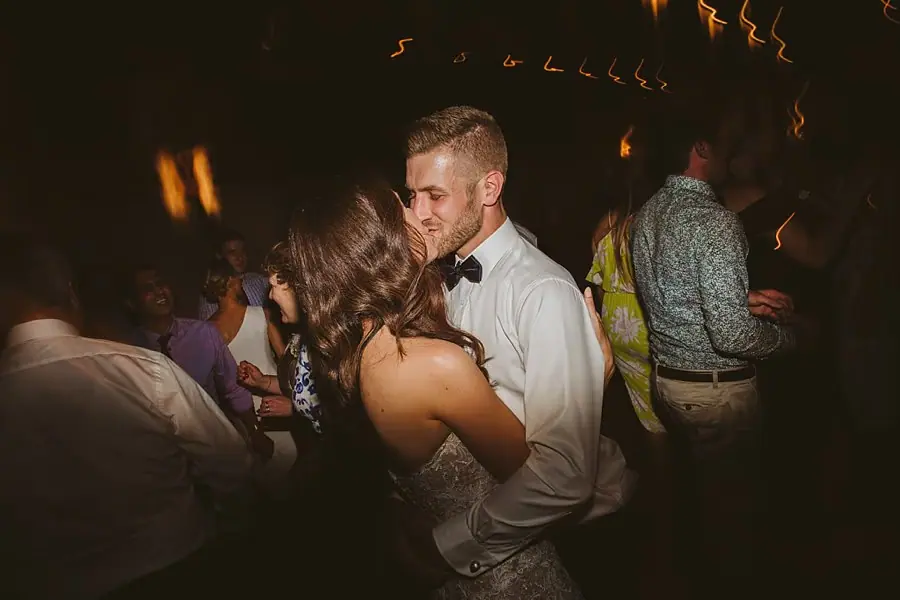 Bride and groom dancing closely among guests at the evening reception.