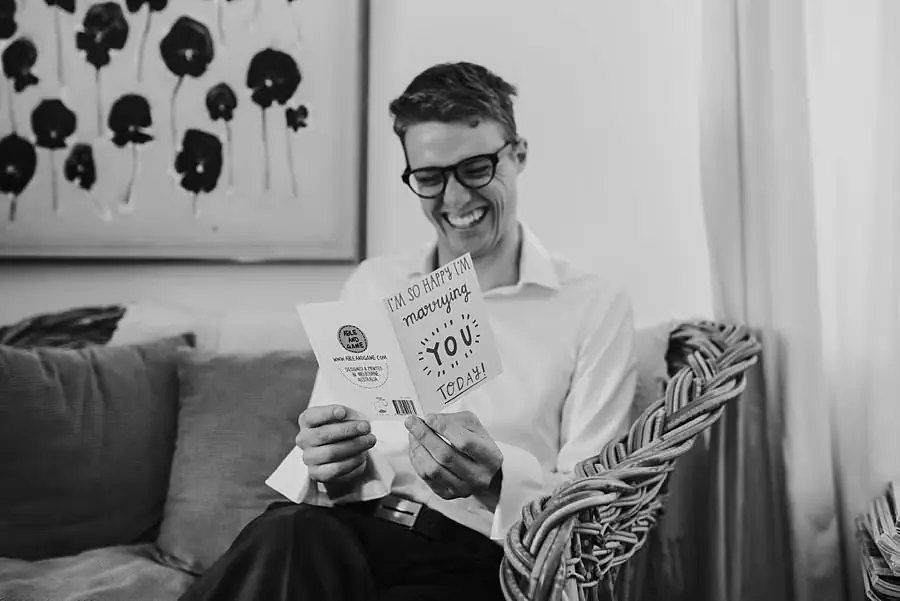 Black-and-white photograph of the smiling groom reading a card
