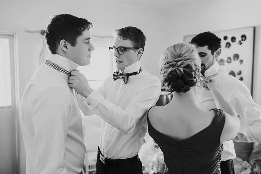 Black-and-white photograph of friends helping adjust bow ties while getting ready