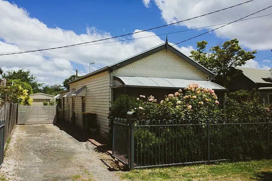 Weatherboard house behind a garden fence and flowering shrubs