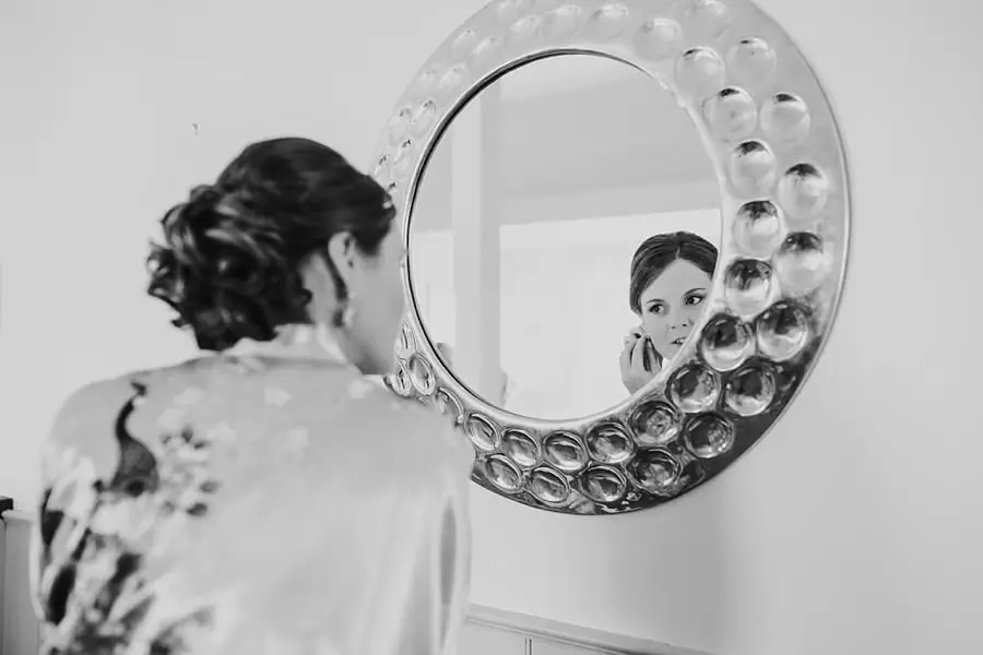 Black-and-white photograph of a woman looking into a round wall mirror
