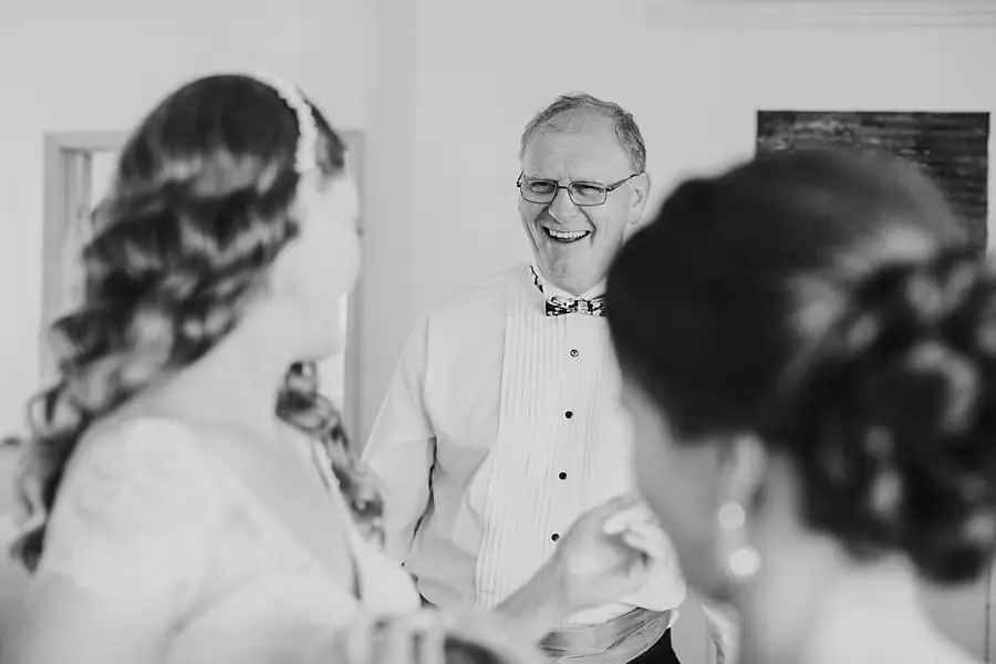 Black-and-white photograph of a smiling older man greeting women indoors