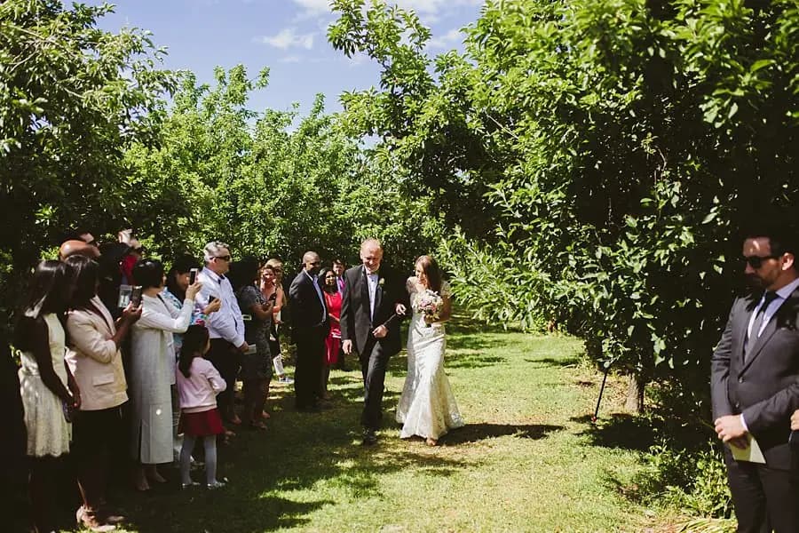 Bride walking with a man through the garden toward waiting guests