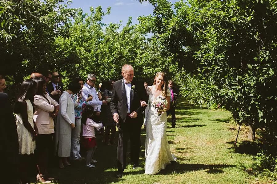 Bride holding her bouquet while walking beside a man between standing guests