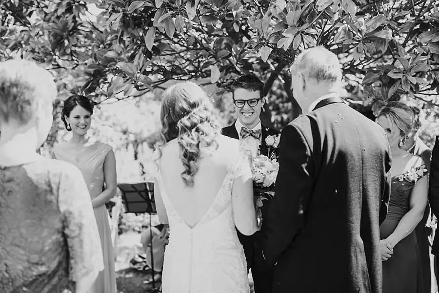 Black-and-white photograph of the wedding party gathered beneath leafy branches