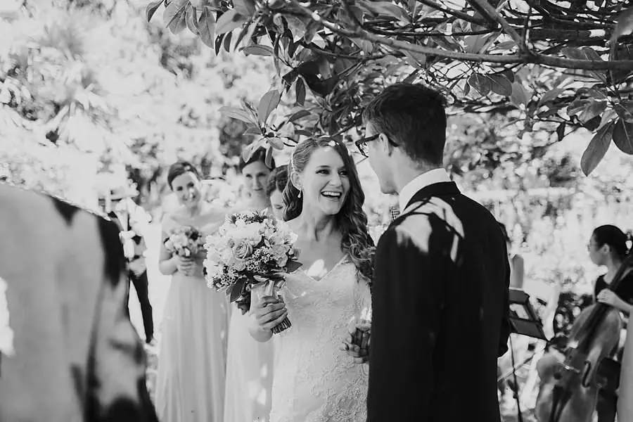 Black-and-white photograph of the bride laughing toward the groom during the ceremony