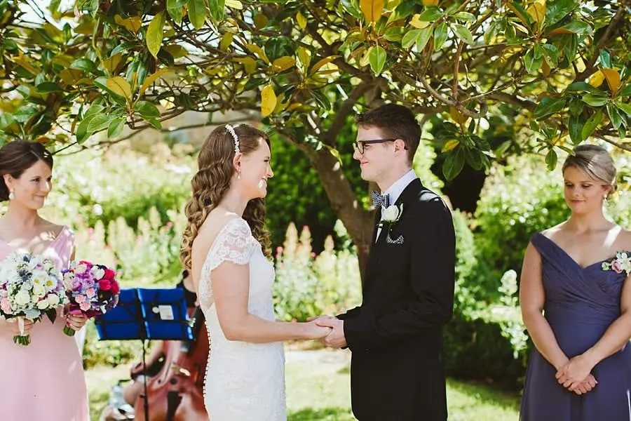 Bride and groom holding hands and facing one another during their garden ceremony