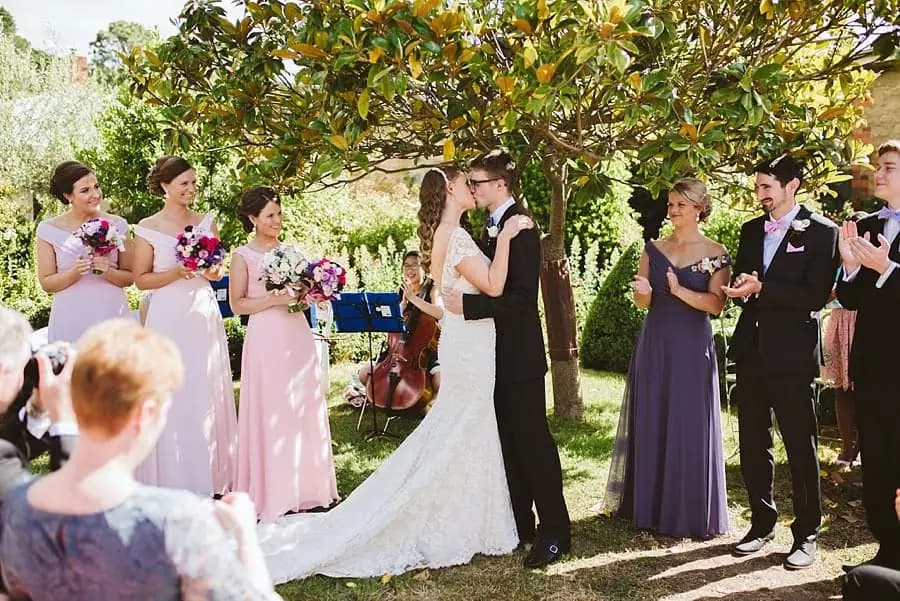 Bride and groom kissing while their wedding party applauds