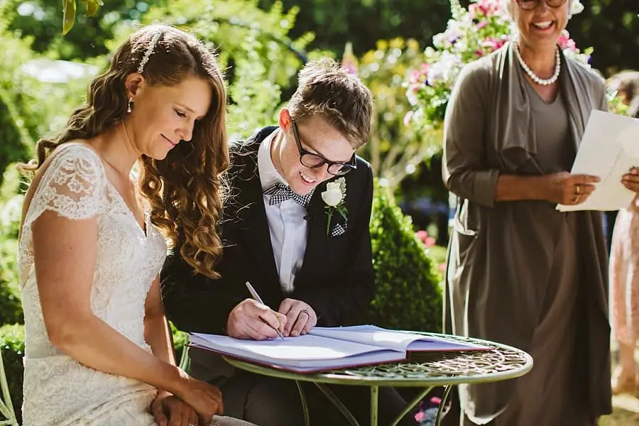 Groom signing the marriage register beside the smiling bride and celebrant