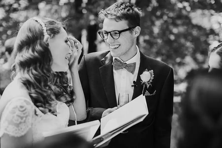 Black-and-white photograph of the bride laughing with the groom beside an open register