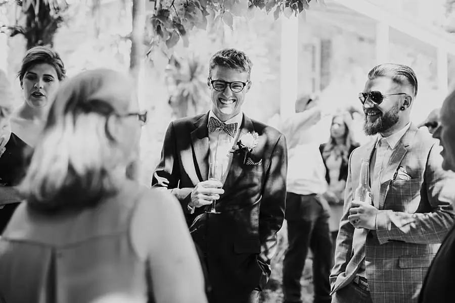 Black-and-white photograph of the groom chatting with guests holding drinks
