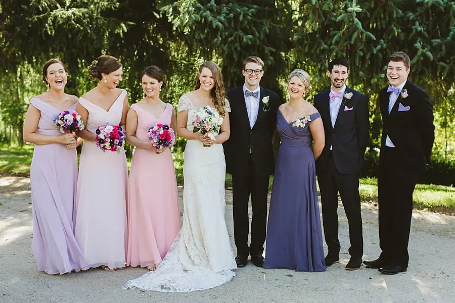 Wedding party posing together beneath trees with colourful bouquets