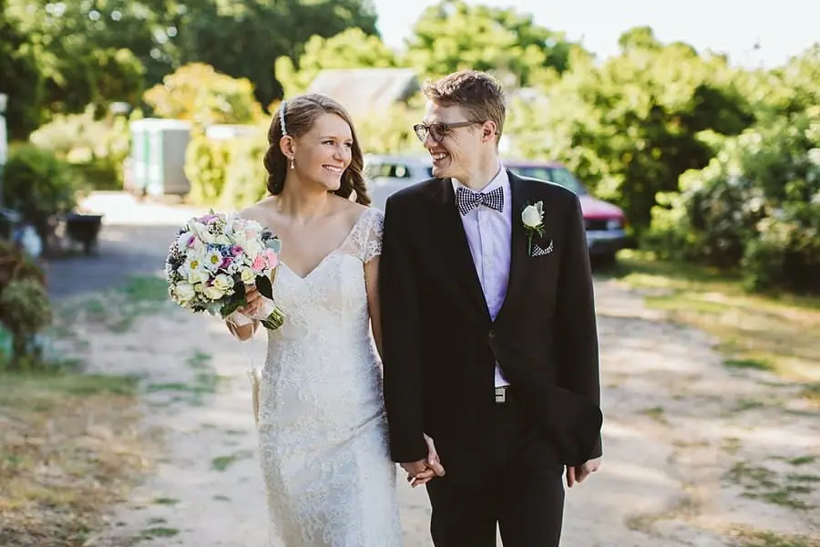 Bride and groom walking hand in hand through the sunny grounds