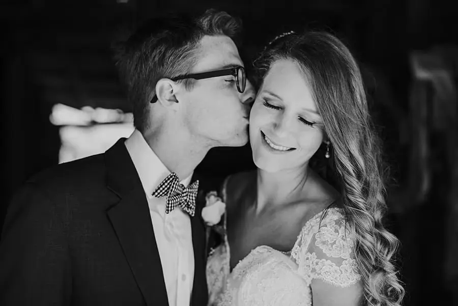 Black-and-white photograph of the groom kissing the bride's forehead