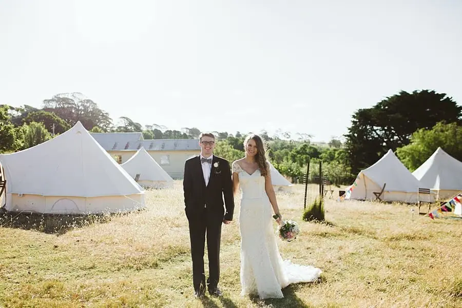Bride and groom walking hand in hand between white bell tents