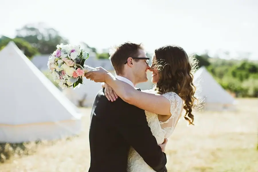 Bride and groom kissing among sunlit white tents
