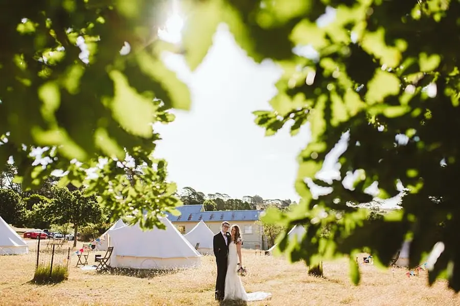 Bride and groom standing in the campsite, viewed through leafy branches