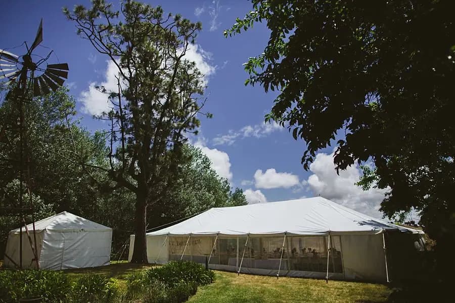 White reception marquee beneath trees and a bright blue sky