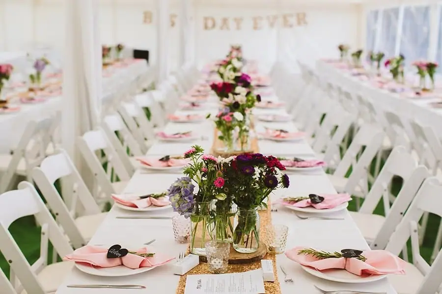 Long reception table lined with flowers, pink napkins and white chairs
