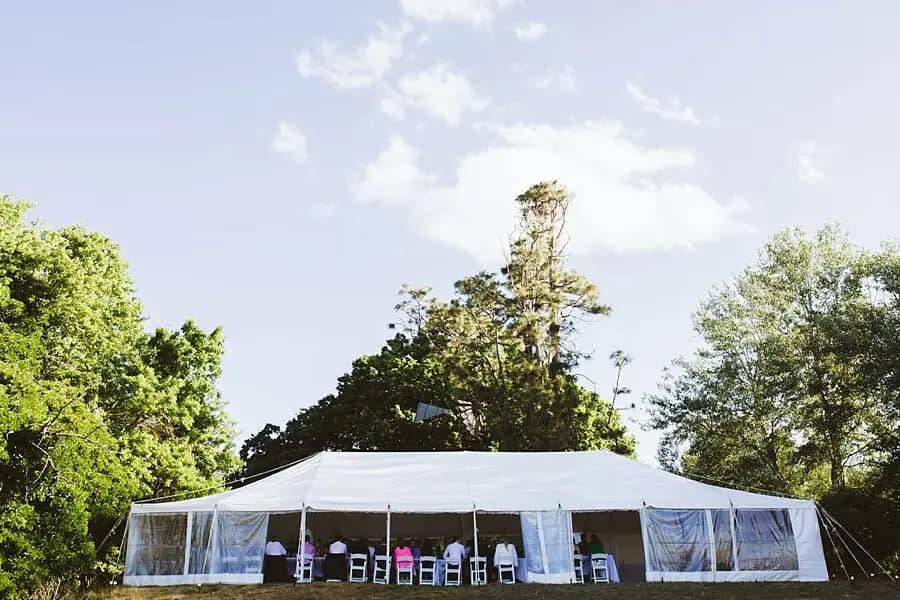 Wide view of the white reception marquee surrounded by tall trees