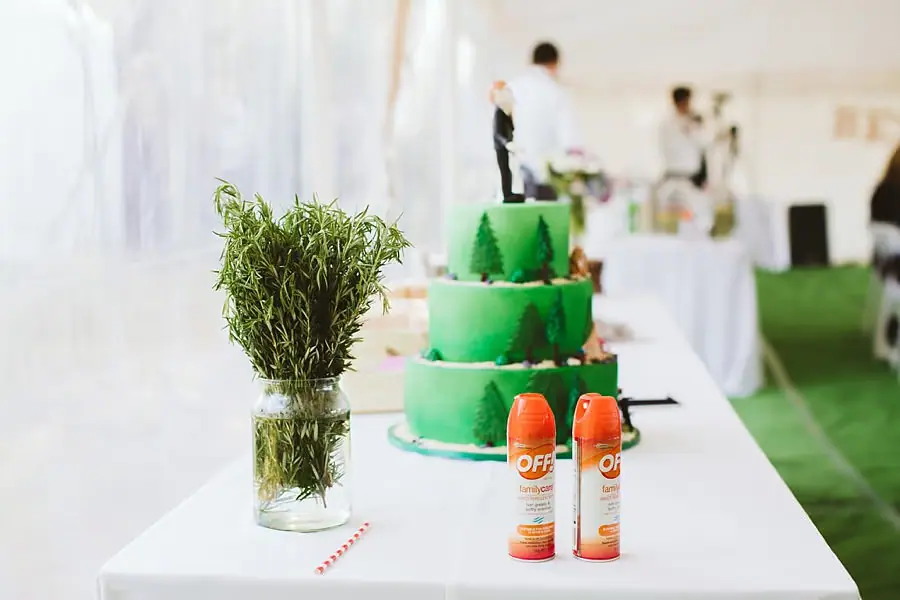 Green wedding cake and a jar of rosemary beside two orange insect-repellent cans