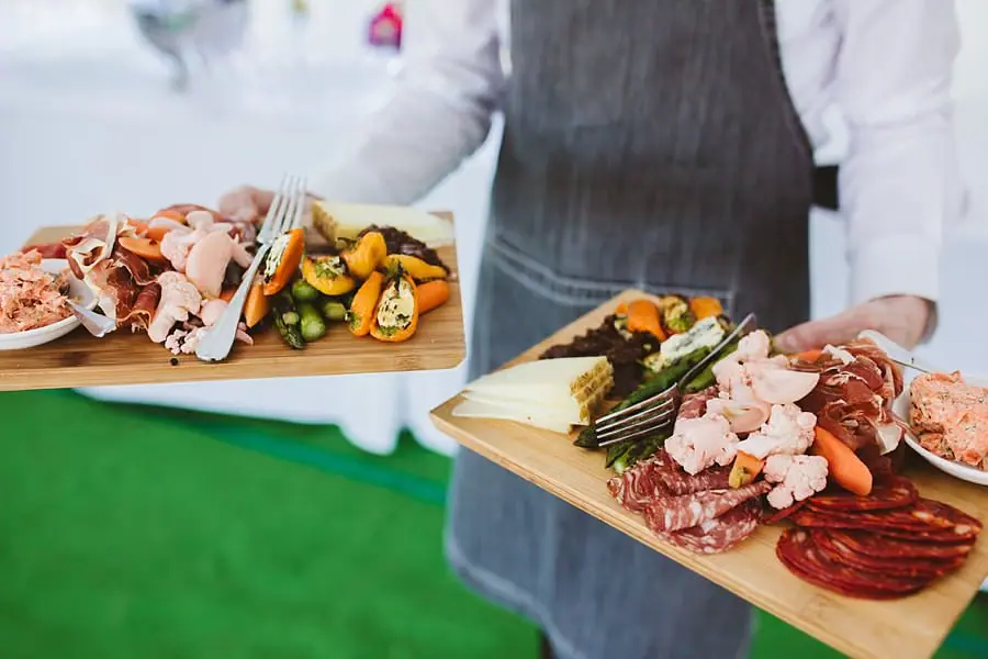 Server carrying wooden boards of food with cured meats and vegetables