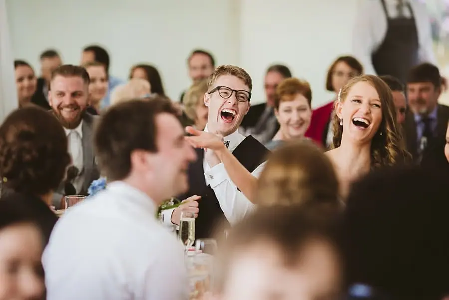 Bride and groom laughing among seated reception guests