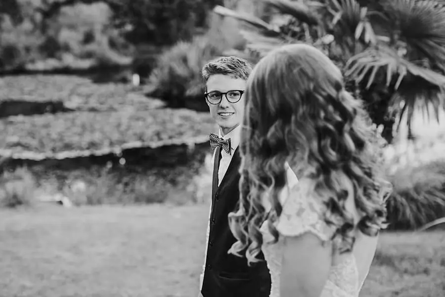 Black-and-white photograph of the groom facing the bride beside a garden pond