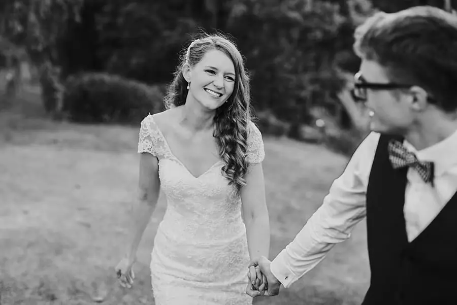 Black-and-white photograph of the bride holding the groom's hand outdoors