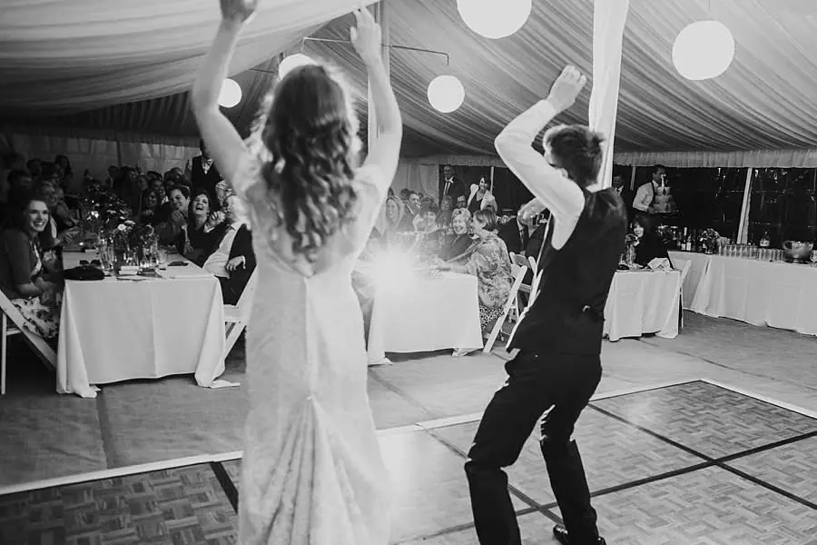 Black-and-white photograph of the bride and a guest dancing with raised arms