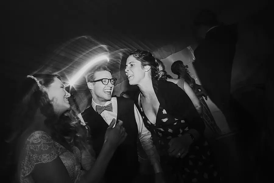 Black-and-white photograph of the groom dancing closely with two guests