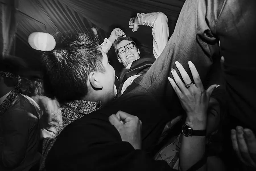 Black-and-white photograph of guests lifting the groom into the air