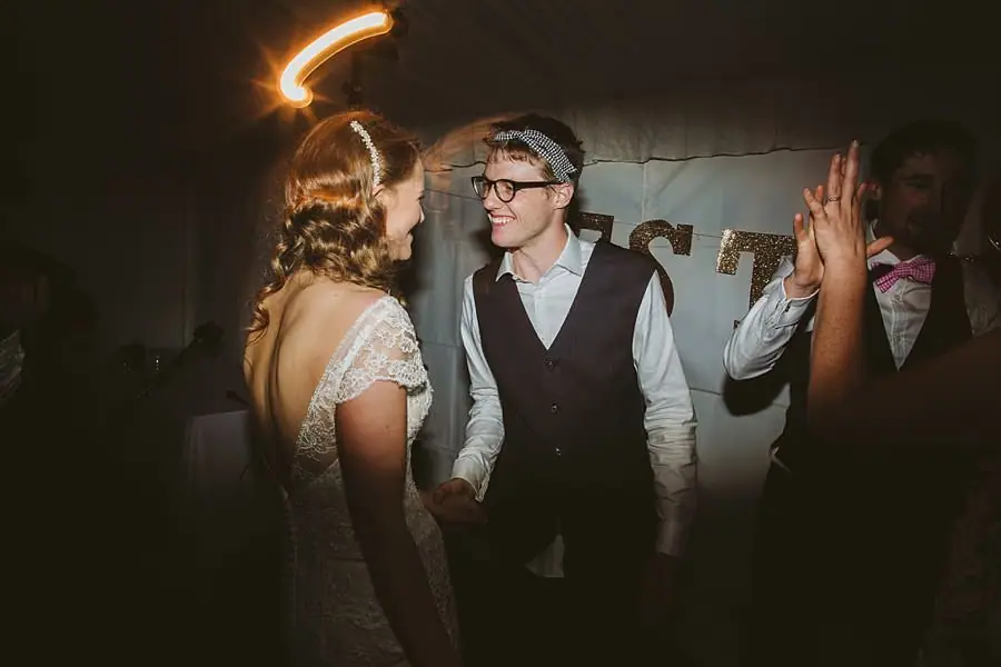 Bride and groom gesturing toward one another while dancing beneath warm light trails